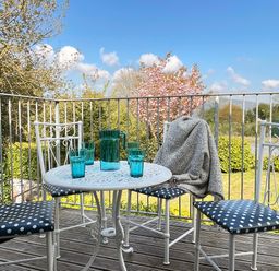 A balcony with a white table and four white chairs with polka dot cushions and a grey blanket on one chair at The Coach House in Llanrwst