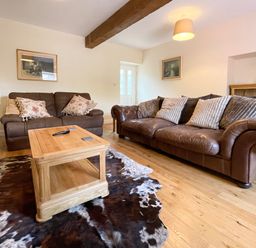 A living room with two brown leather sofas a wooden coffee table a cowhide rug and paintings on the walls at The Coach House in Llanrwst