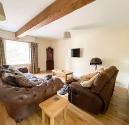 A living room with brown leather sofas a wooden coffee table a cowhide rug a wall-mounted TV and a wooden beam on the ceiling at The Coach House in Llanrwst