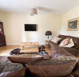 A living room with brown sofas a wooden coffee table a mounted tv and a corner cabinet at The Coach House in Llanrwst
