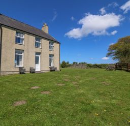 A large two-story house with a green lawn and outdoor chairs next to a wooden fence at Ty Mawr in Llanddaniel Fab