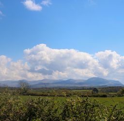 A landscape with green fields bushes and mountains under a blue sky with clouds at Ty Mawr in Llanddaniel Fab