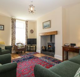 A living room with a wood burning stove a television floral curtains and patterned rugs at Ty Mawr in Llanddaniel Fab