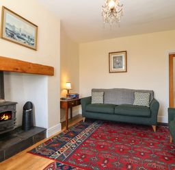 A living room with a red patterned rug a green sofa and armchair a wood burning stove and framed paintings at Ty Mawr in Llanddaniel Fab