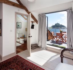 A bedroom with bunk beds and a metal bed frame next to a balcony overlooking water and a castle at Star House in Marazion