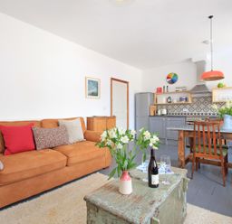 A living room with a brown sofa red and patterned cushions a wooden dining table with chairs and flowers in vases at Star House in Marazion