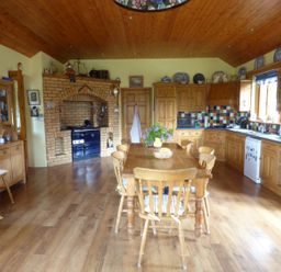 A kitchen with a wooden dining table and chairs a brick oven wooden cabinets and tiled backsplash at Maifield in Carrick-On-Suir County Tipperary