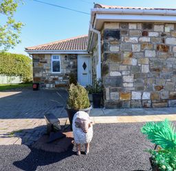 An outdoor area with a stone wall and sheep statue at Blacksmiths Cottage in Shilbottle