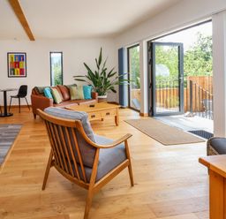 A living room with a wooden armchair a brown sofa a wooden coffee table and a small dining table with two black chairs at No1 The Lodge in Acton near Bishops Castle