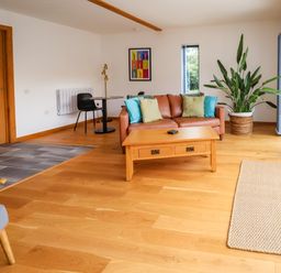 A living room with a brown sofa with cushions a wooden coffee table a black chair a small round table a large plant and wooden flooring at No1 The Lodge Acton near Bishops Castle