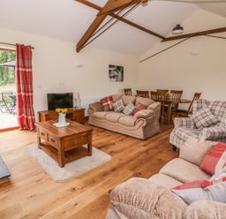 A living room with sofas cushions a wooden coffee table tv and a dining table with chairs at Pentre Fach in Llandrindod Wells