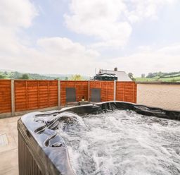 An outdoor hot tub with water jets and two chairs with a table behind it at Pentre Fach in Llandrindod Wells