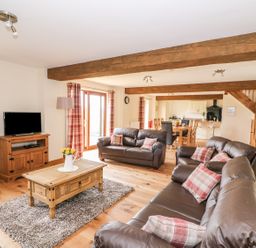 A living room with brown leather sofas and a wooden coffee table with flowers at Pentre Fawr in Llandrindod Wells