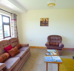 A living room with sofa and armchair a wooden coffee table and window with floral curtains at Nephin View in Foxford County Mayo