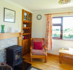 A living room with an armchair by a wood stove and a window at Nephin View in Foxford County Mayo