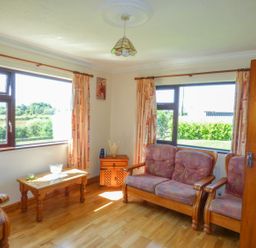 A sitting room with wooden furniture including a sofa armchair and coffee table and two large windows at Nephin View in Foxford County Mayo