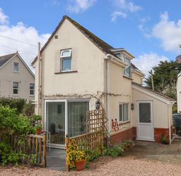 The back of a two story cream house with a wooden deck and potted plants at Wisteria Cottage in Exmouth