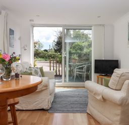 A living room with armchairs table with flowers television and sliding glass door leading outside at Wisteria Cottage in Exmouth