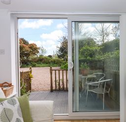 A living area opening to a garden through sliding glass doors with a small outdoor table and chairs at Wisteria Cottage in Exmouth