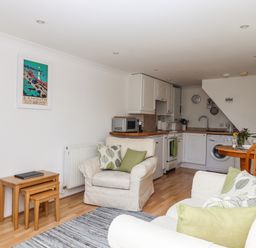 A living room with sofa and armchair next to a kitchen with white cabinets and wooden fixtures at Wisteria Cottage in Exmouth