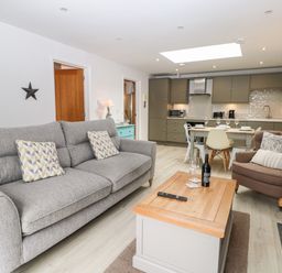 An open living room and kitchen with a gray sofa, brown armchair, wooden coffee table, and dining table with chairs at Rabbits Warren in Titchfield Common