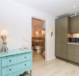 A kitchen with gray cabinets a microwave and a turquoise dresser with a rabbit lamp next to a bathroom at Rabbits Warren in Titchfield Common
