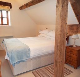 A bedroom with a double bed wooden furniture and visible wooden beams at The Granary Walford near Ross-on-Wye