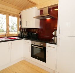 A kitchen with white cabinets a black countertop a red backsplash and wooden window frames at The Shippen in Merriott
