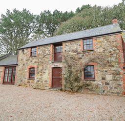 A stone cottage with multiple windows and wooden doors surrounded by trees at Barn Cottage in Marazion