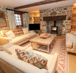 A living room with stone walls two sofas an armchair a wooden coffee table and a fireplace with a wood stove at Barn Cottage in Marazion