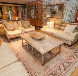 A sitting area with armchairs sofas a wooden coffee table and a cabinet in a room with stone walls and a window at Barn Cottage in Marazion