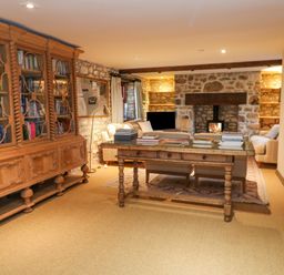 A living room with a large wooden bookshelf a table with books and a stone fireplace at Barn Cottage in Marazion