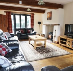 A living room with black leather sofas a wooden coffee table a TV on a wooden stand and a fireplace at Carthorse Cottage in Teignmouth