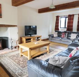 A living room with leather sofas a wooden coffee table a fireplace a television and wooden beams on the ceiling at Carthorse Cottage in Teignmouth