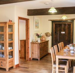 A dining room with a wooden table and chairs a cabinet with glassware a sideboard with flowers and a wooden door at Carthorse Cottage in Teignmouth
