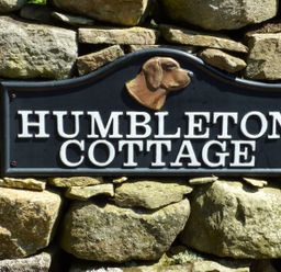 A stone wall with a sign that reads HUMBLETON COTTAGE with a dog head sculpture above the text at Humbleton Cottage in Haydon Bridge near Hexham