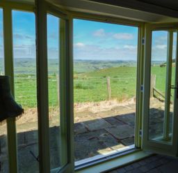 A view through open glass doors showing a grassy patio and a fence with hills and fields beyond at Humbleton Cottage in Haydon Bridge near Hexham