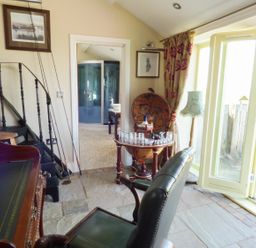 A room with a wooden desk chair and a round bar cabinet near a glass door at Humbleton Cottage in Haydon Bridge near Hexham
