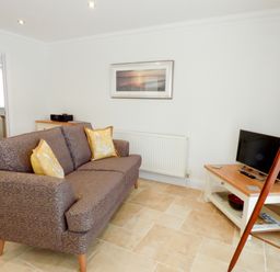 A living room with a sofa pillows television and a tripod lamp at The Hideaway in Verwood