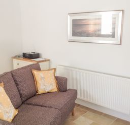 A room with a patterned couch with yellow pillows beside a white radiator and a small cabinet with a radio on top at The Hideaway in Verwood