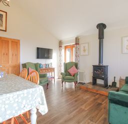 A living room with a dining table wooden chairs green armchairs a wood stove and a wall mounted television at Stoney-Brook Lodge in Bedlam near Ludlow