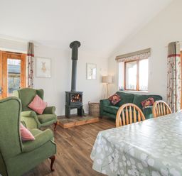 A living room with green armchairs a wood burning stove and a dining table at Stoney-Brook Lodge in Bedlam near Ludlow