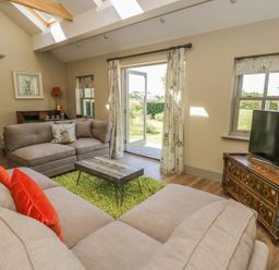 A living room with beige sofas a wooden coffee table green rug and a television on a wooden cabinet at Providence Cottage in Easingwold