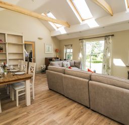 A living room with a dining table set for six people a bookshelf two sofas a television and skylight windows at Providence Cottage in Easingwold