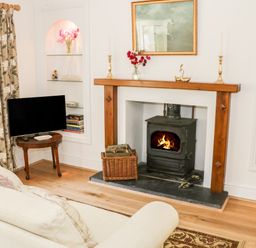 A living room with a wood burning stove fireplace a television on a wooden table and bookshelves at Coachmans Cottage in Witherslack
