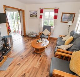 A living room with wooden floor a grey leather sofa and armchair a wooden coffee table and a fireplace at Lough Mask Road Fishing Cottage in Ballinrobe County Mayo
