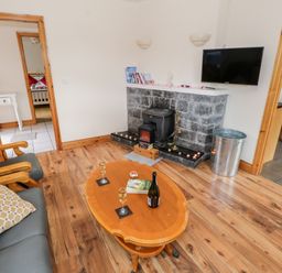 A living room with wooden floor a fireplace and a coffee table with drinks and a book at Lough Mask Road Fishing Cottage in Ballinrobe County Mayo