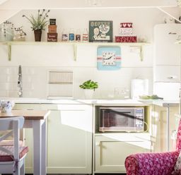 A kitchen with a microwave in a cabinet and a red chair at The Snug in Rescorla near St Austell
