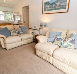 A living room with two cream sofas with cushions a lamp on a side table and a kitchen area with a window and sink at Brook Haven Rosecraddoc Lodge near Liskeard Cornwall