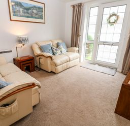 A living room with two beige sofas a wooden side table a lamp a painting on the wall and a door with windows at Brook Haven Rosecraddoc Lodge near Liskeard Cornwall